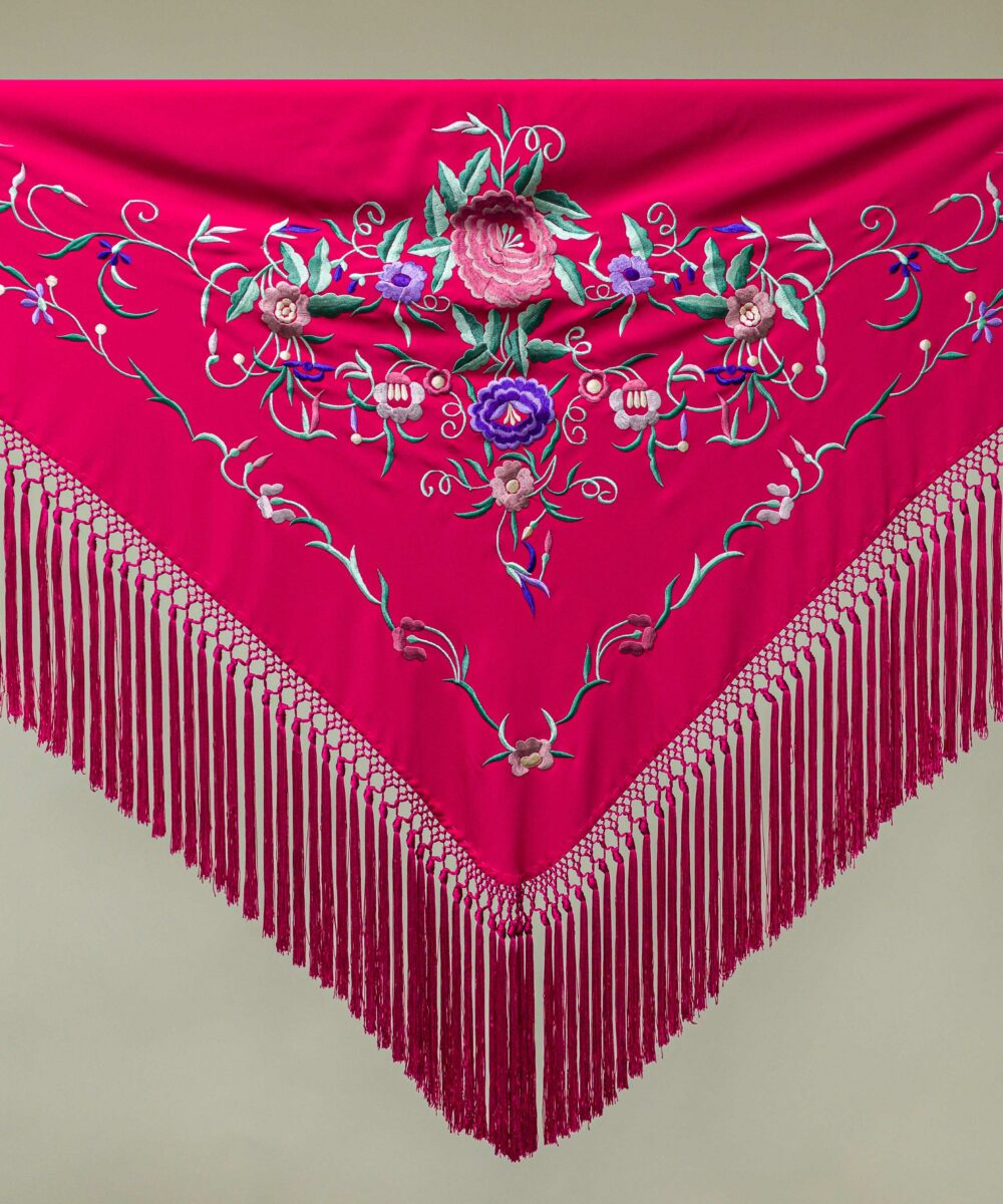 El mantoncillo bordado en crespón fucsia es un básico, puedes combinar nuestro mantón bordado con varios colores de vestido y flores de flamenca.